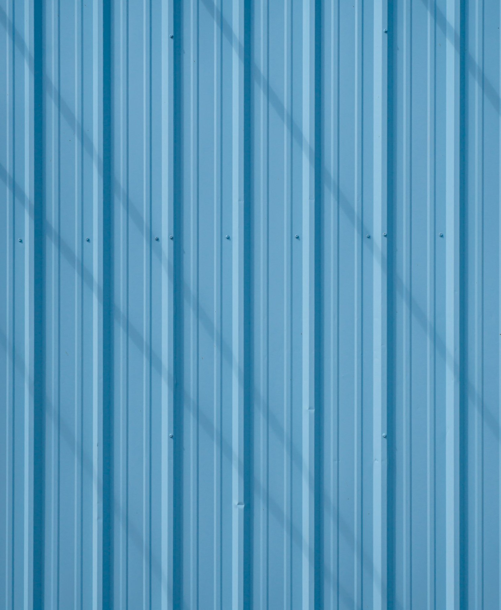 Close-up of a coated blue corrugated steel privacy panel with vertical ribs and fasteners